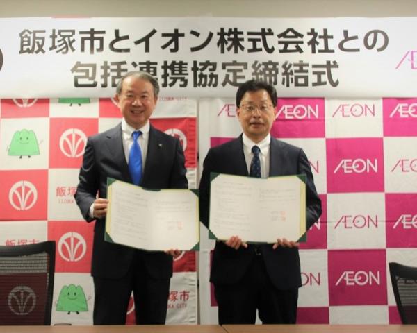 締結式の署名を終え起立する武井市長とイオン九州株式会社の中川社長