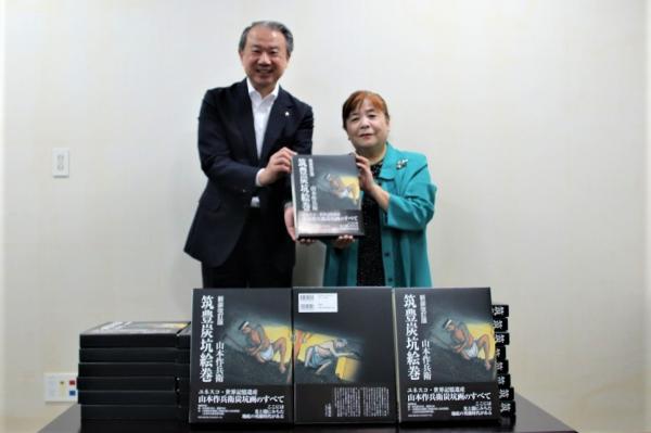 市長と一緒に山本作兵衛氏の書籍を持つ寄贈者の緒方さん