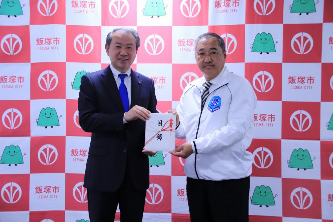 寄附金贈呈式で目録を手にする松本実行委員長と武井市長