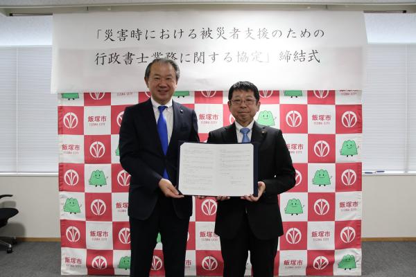 締結式で福岡県行政書士会の田村公隆会長および武井市長が協定書をもって写真におさまる。